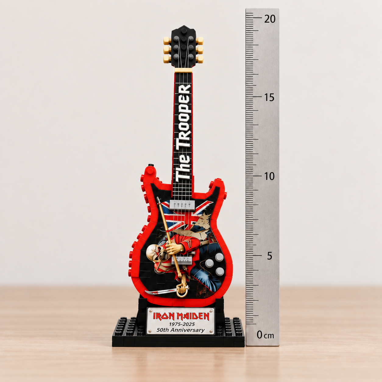 Miniatura da guitarra Iron Maiden The Trooper ao lado de uma r&eacute;gua em cent&iacute;metros, mostrando as dimens&otilde;es aproximadas de 19,5 &times; 6,5 &times; 10 cm.